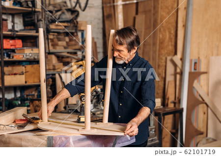 Mature carpenter measures the length of a table with a tape Mature carpenter measures the length of a table with a tape 62101719