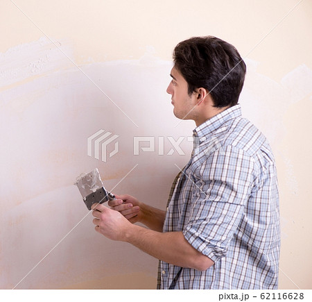 Young man applying plaster on wall at home Young man applying plaster on wall at home 62116628