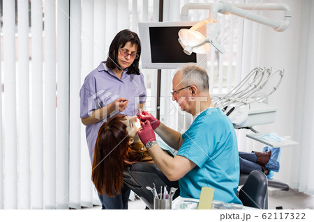 Medical dentist team in modern dental office doing treatment of tooth for female young patient. Senior male dentist and his assistant working in modern dental clinic 62117322