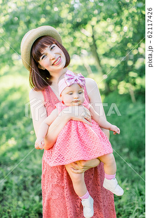 Beautiful Mother with the straw hat And her little daughter outdoors family look in in a pink dress . Young mother with her little baby on the meadow 62117426
