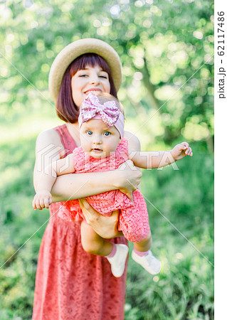 Beautiful Mother with the straw hat And her little daughter outdoors family look in in a pink dress . Outdoor Portrait of happy family. family look. Happy mother having fun with her daughter 62117486