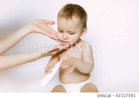 Woman applying body cream on her baby against light background Woman applying body cream on her baby against light background 62117561