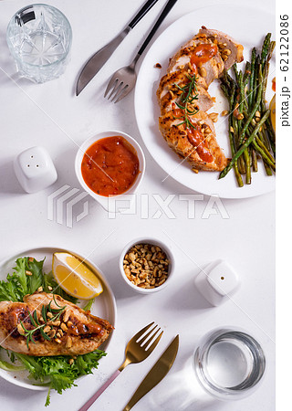 Grilled chicken breast with grilled asparagus and lemon slice, peanuts and sauce on white stone background . Paleo diet. Grilled chicken breast with grilled asparagus and lemon slice, peanuts and sauce on white stone background . Paleo diet. 62122086