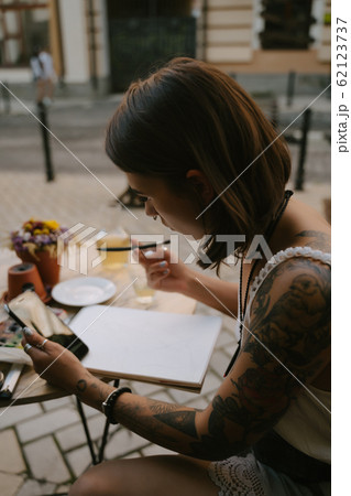 Young woman draws at the sketchbook with a pencil outdoors on the street Young woman draws at the sketchbook with a pencil outdoors on the street 62123737