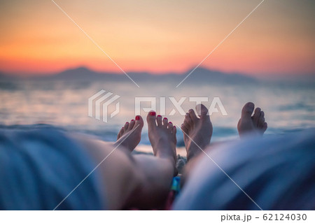 Legs on beach. A young loving couple hugging and kissing on the beach at sunset. Two lovers, man and woman barefoot near the water. In summer. 62124030