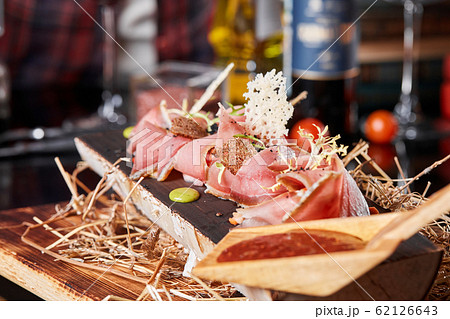 Antipasto on wooden plate close up. Cold smoked meat plate with tomato hot sauce, sliced ham, prosciutto, bacon. Appetizer on wooden tray cut tree sawed imitation. Antipasto on wooden plate close up. Cold smoked meat plate with tomato hot sauce, sliced ham, prosciutto, bacon. Appetizer on wooden tray cut tree sawed imitation. 62126643