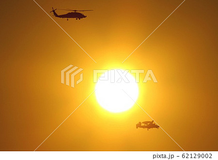 美しい夕日を背景に飛行する米海軍の艦載機SH-60Bシーホーク哨戒ヘリとE-2Cホークアイ早期警戒機 62129002