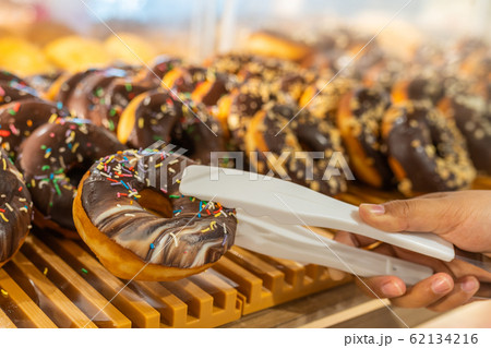 Human hand using clamp picking chocolate donut at pastry shop 62134216