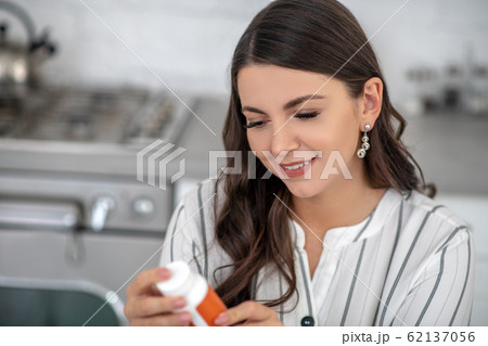 Long-haired woman in a striped blouse holding a jar of vitamins in her hands Long-haired woman in a striped blouse holding a jar of vitamins in her hands 62137056