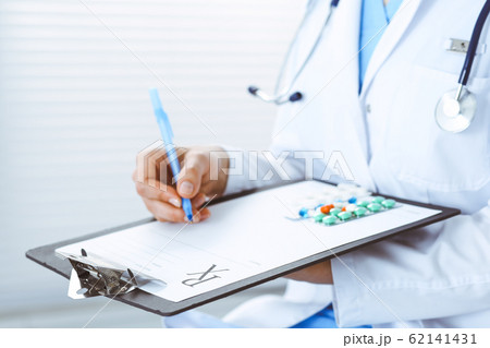 Unknown woman doctor at work at hospital. Pills at medical clipboard. Young female physician write prescription or filling up medical form while sitting in hospital office, close-up 62141431