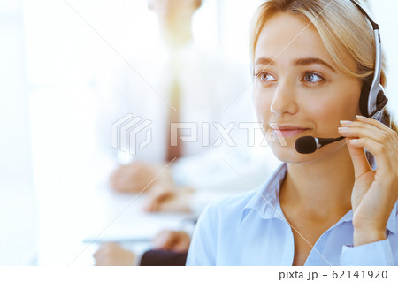 Group of diverse phone operators at work in sunny office. Handsome business woman with headphones consulting clients. Call center and business people concept 62141920