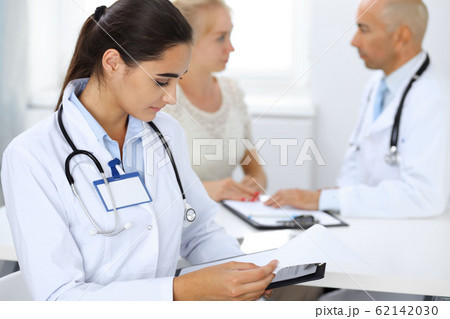Doctor woman in clinic with colleagues at the background. Hispanic or latin american staff in medicine Doctor woman in clinic with colleagues at the background. Hispanic or latin american staff in medicine 62142030
