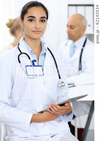 Doctor woman in clinic with colleagues at the background. Hispanic or latin american staff in medicine Doctor woman in clinic with colleagues at the background. Hispanic or latin american staff in medicine 62142034