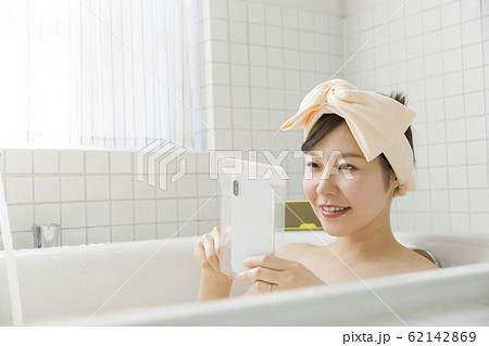 バスルームで防水ケースにスマホを入れて観覧する若い女性 62142869