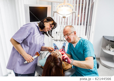 team of two doctors dentists, senior man and woman, treating young female patient in a dental clinic 62144566