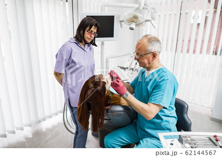 Oral care and dentistry concept. Senior concentrated male doctor with his female nurse assistant inspecting woman patient teeth. 62144567