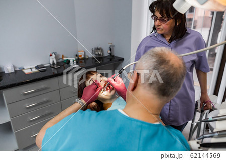 Female patient with senior man doctor dentist and his female assistant doing dental treatment in modern clinic 62144569