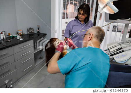 Female patient with open mouth during drilling treatment at the dentist. Professional dental team man and woman doing treatment for young woman patient 62144570