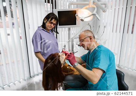 Medical dentist team in modern dental office doing treatment of tooth for female young patient. Senior male dentist and his assistant working in modern dental clinic 62144571