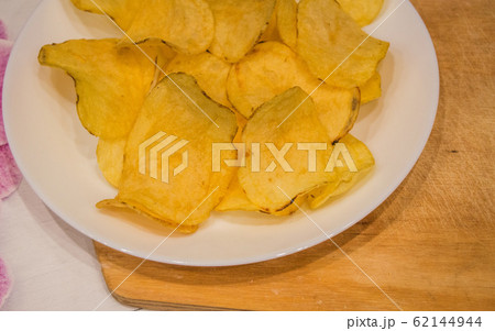 Delicious potato chips round shape, on a white plate on the background of a light wooden table, top view Delicious potato chips round shape, on a white plate on the background of a light wooden table, top view 62144944