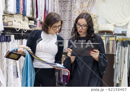Female salesman and buyer in the fabric store are looking to select samples of materials Female salesman and buyer in the fabric store are looking to select samples of materials 62150407
