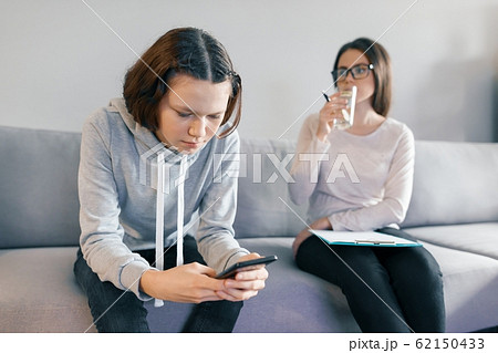 Teenager patient girl talking with professional psychotherapist in office. Girl looks into her phone ignores a psychologist. Teenager patient girl talking with professional psychotherapist in office. Girl looks into her phone ignores a psychologist. 62150433