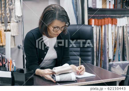 Workplace female designer, business woman in glasses with notebook pen and sample of fabric working in the office Workplace female designer, business woman in glasses with notebook pen and sample of fabric working in the office 62150443