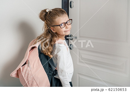 Little pretty girl 6, 7 years old with school backpack. Smiling girl standing near the front door of the house, child goes to school 62150653
