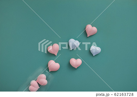 pink and two blue meringue hearts in transparent glass goblet and scattered on turquoise background diagonally, copy space 62163728