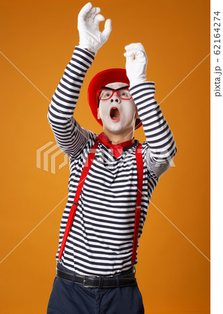 Young mime male in white gloves and red hat looking up on orange background Young mime male in white gloves and red hat looking up on orange background 62164274