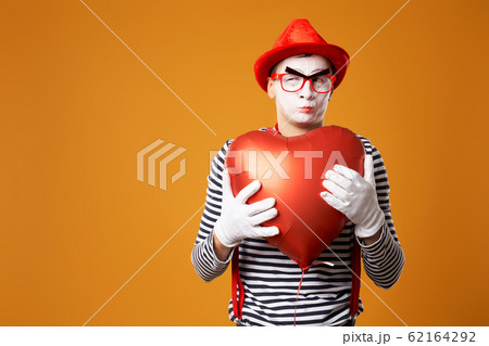 Close up mime in red hat and vest holds heart ball in his hands 62164292