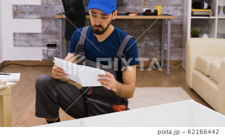 Confused worker in overalls reading instructions Confused worker in overalls reading instructions 62166442