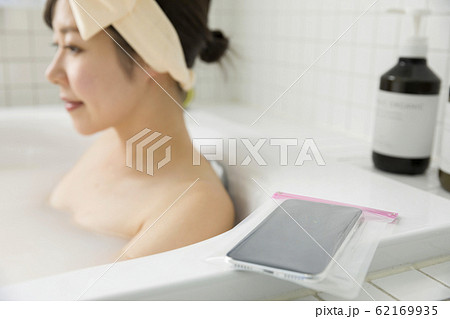 バスルームに防水ケース入りスマホを持ち込む若い女性 62169935