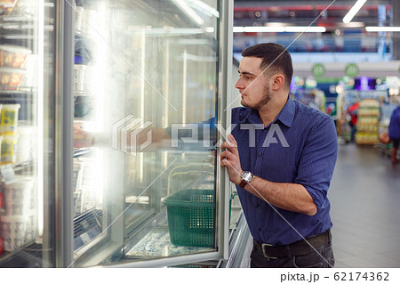 Man in a supermarket standing in front of the freezer looking for his favorite frozen food. Man in a supermarket standing in front of the freezer looking for his favorite frozen food. 62174362