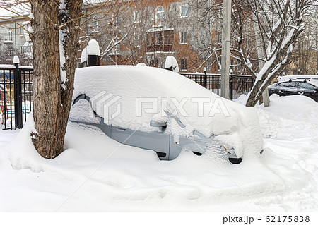 Close-up one completely snowbound grey car is standing fixedly in snowdrift in yard house. Winter cityscape. Close-up one completely snowbound grey car is standing fixedly in snowdrift in yard house. Winter cityscape. 62175838