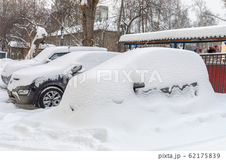 Heavily snowbound cars are standing fixedly in snow in yard house. Winter cityscape. Heavily snowbound cars are standing fixedly in snow in yard house. Winter cityscape. 62175839