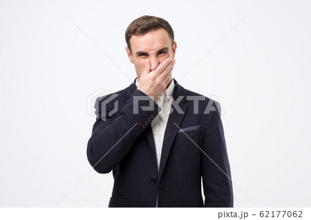 Young man in suit closing nose due to bad smell 62177062