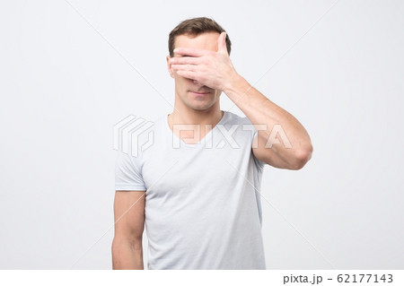 Young caucasian man closes his eyes with his hands Young caucasian man closes his eyes with his hands 62177143