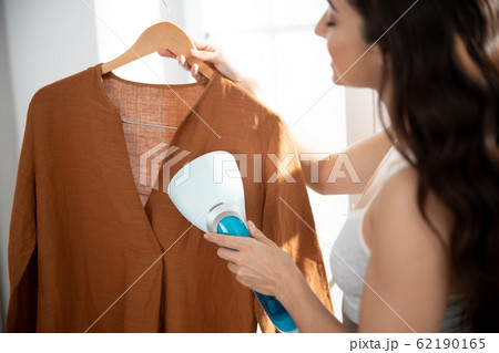Young lady using clothes steamer to freshen up shirt 62190165