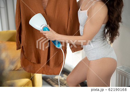 Young woman using electric handheld clothes steamer Young woman using electric handheld clothes steamer 62190168