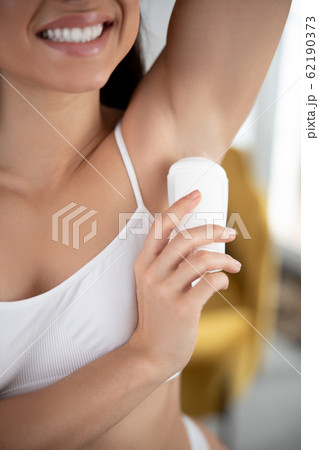 Joyful young woman applying antiperspirant on armpit 62190373
