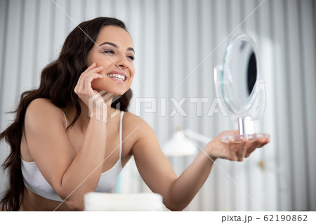 Charming lady touching face and looking in the mirror Charming lady touching face and looking in the mirror 62190862