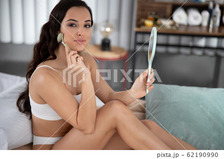 Beautiful young woman using face massager in bedroom Beautiful young woman using face massager in bedroom 62190990