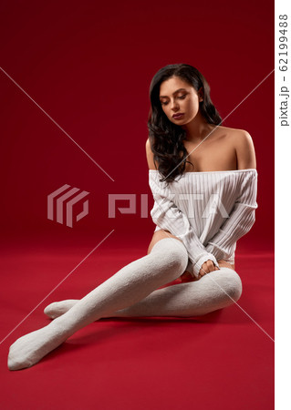 Brunette model posing on floor in sweater. 62199488