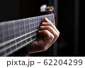 Female hand clamps a chord on an acoustic guitar 62204299