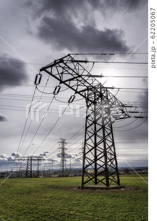 Sun hidden behind dramatic clouds and electricity pylons conducting current from distribution power station, solar renewable energy and grid stability concept, copy space Sun hidden behind dramatic clouds and electricity pylons conducting current from distribution power station, solar renewable energy and grid stability concept, copy space 62205067