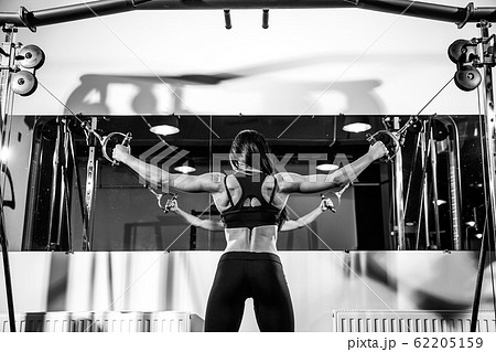woman flexing muscles on cable machine in gym. exercise on biceps. back view woman flexing muscles on cable machine in gym. exercise on biceps. back view 62205159