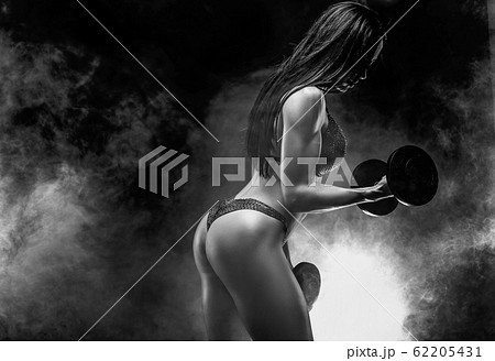 Muscular unrecognizable brunette in bikini doing exercise on biceps with dumbbells in smoke Muscular unrecognizable brunette in bikini doing exercise on biceps with dumbbells in smoke 62205431