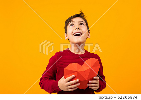 funny cheerful handsome caucasian boy with paper heart for valentines day on orange background 62206874