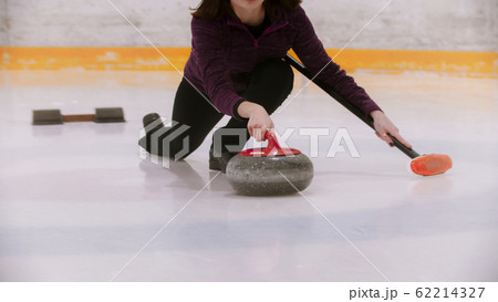 Curling training - woman skating holding a granite stone with red handle 62214327